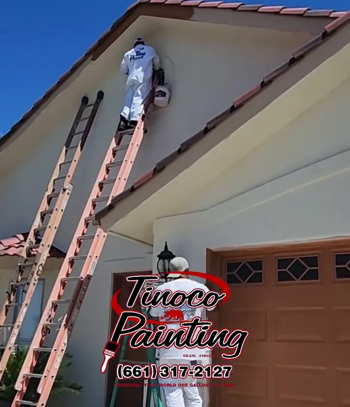 Two ladders against a tile-roofed Bakersfield house with a Tinoco Painting crew member working on the gable